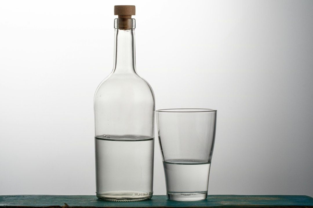 Glasflaska med kork och glas, båda delvis fyllda med klar vätska
